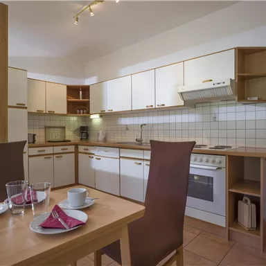 Eine moderne Küche mit hellen Möbeln und genügend Stauraum. Der Tisch ist gedeckt, bereit für eine Mahlzeit.
