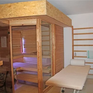 Ein stilvolles Saunaraum mit Glasfront und Holzdetails. Neben der Sauna befindet sich eine Liege und ein Gestell für Handtücher.