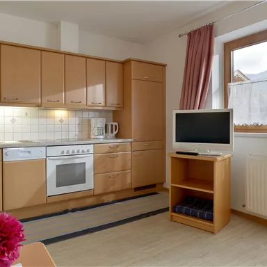 Eine helle Küche mit Holzschränken und modernen Geräten. Im Raum steht ein Fernseher und es gibt ein großes Fenster mit Ausblick.