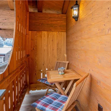 Ein gemütlicher Balkon mit Holzmöbeln und einer Laterne. Die Holzverkleidung schafft eine warme und einladende Atmosphäre.