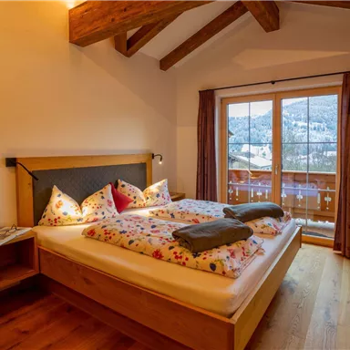 Ein gemütliches Schlafzimmer mit Holzvertäfelung und einem großen Doppelbett. Große Fenster bieten einen schönen Blick auf die Natur.