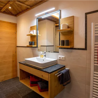 Ein modernes Badezimmer mit Holzdetails und einem eleganten Waschtisch. Der Raum ist hell und gut beleuchtet, mit Handtüchern in verschiedenen Farben.