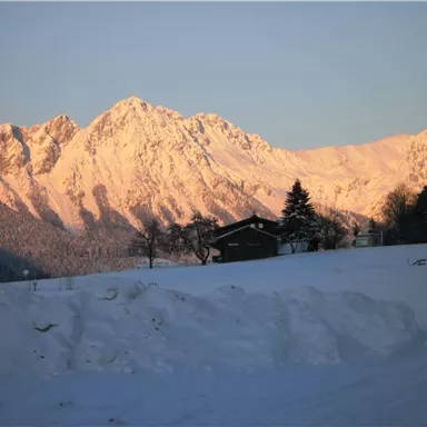 A snowy landscape with snow-covered mountains in the background. In the foreground, there is a wooden house surrounded by snow.