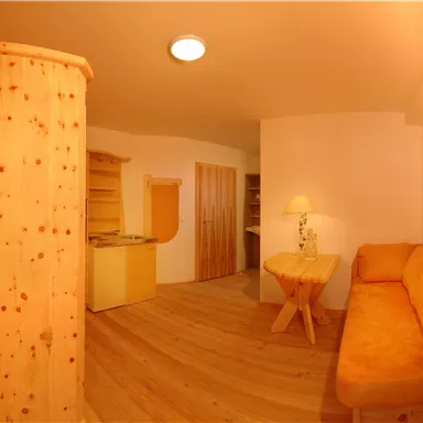 Ein gemütlicher Raum mit einem orangefarbenen Sofa und Holzmöbeln. Die Atmosphäre ist warm und einladend, mit einem Holzfußboden.