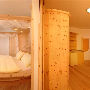 Ein modernes Zimmer mit einem runden Bett aus Holz und einem gemütlichen Wohnbereich. Die warmen Farben und das helle Licht schaffen eine einladende Atmosphäre.