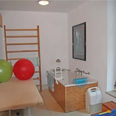Ein modernes Badezimmer mit einer Badewanne und bunten Fitnessbällen. Es gibt auch eine Ablage und große Fenster, die Licht hereinlassen.