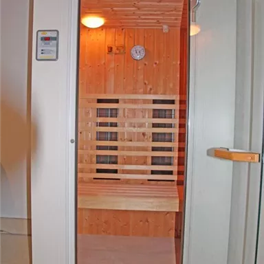 Eine moderne Sauna mit Holzregalen und sanfter Beleuchtung. Die Glasfront bietet einen Blick ins Innere.