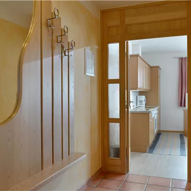 Ein heller Flur mit Holzpaneelen und einem Garderobenständer. Im Hintergrund ist eine offene Küche sichtbar.