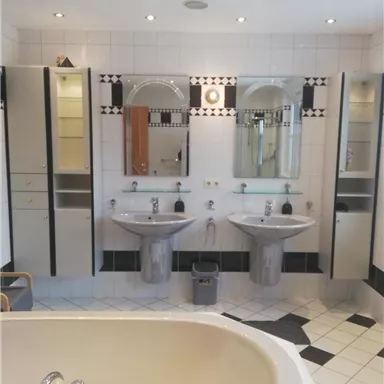 Ein modernes Badezimmer mit einer Badewanne und zwei Waschbecken. Die Wände sind hell gefliest und mit stilvollen Spiegeln und Schränken ausgestattet.