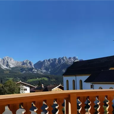 Eine malerische Landschaft mit einem Kirchturm und majestätischen Bergen im Hintergrund. Der Himmel ist klar und blau.