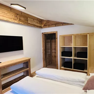 A modern bedroom with wooden paneling and a television on the wall. There is a cozy bed and shelves with dark blue boxes.