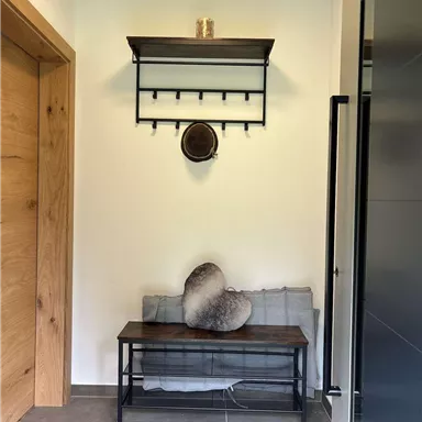 Ein einladender Flur mit einem Holzregal und einer Bank. An der Wand hängen ein paar praktische Haken.