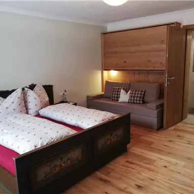 Ein gemütliches Schlafzimmer mit zwei Betten und einem Sofa. Der Boden ist aus Holz, und es gibt warmes Licht sowie Holzdetails im Raum.