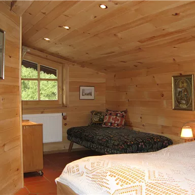 A cozy room with wooden walls and two beds. There is a window with a view outside and a small lamp on the nightstand.