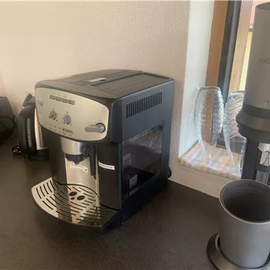 Eine moderne Kaffeemaschine steht auf einer Arbeitsfläche. Im Hintergrund sind ein Toaster und Gläser zu sehen.