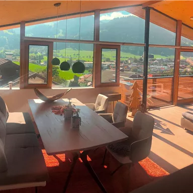Ein modernes Wohnzimmer mit großen Fenstern und Blick auf die Berge. Der Raum ist hell und gemütlich eingerichtet mit einem Esstisch und komfortablen Stühlen.