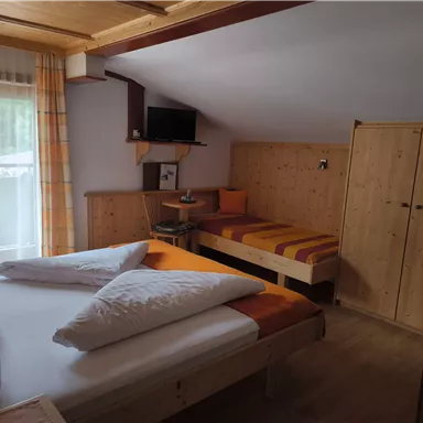A cozy room with a large double bed and a single bed. Wooden paneling and orange accents create an inviting atmosphere.