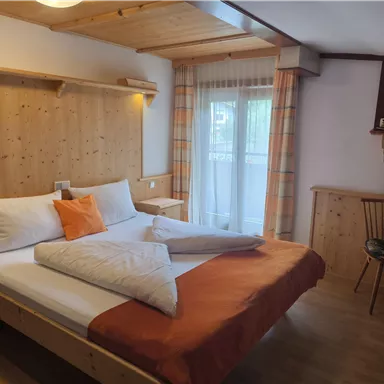 A cozy bedroom with a wooden ceiling and a large bed. The room is bright and friendly, with a small table and chair.