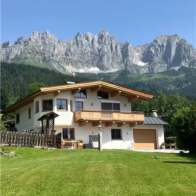 A beautiful house in the Alps with a well-kept garden. In the background, majestic mountains rise up under a clear blue sky.