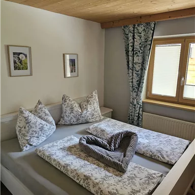 A cozy bedroom with a large bed and decorative pillows. Bright walls and a window let in a lot of light.
