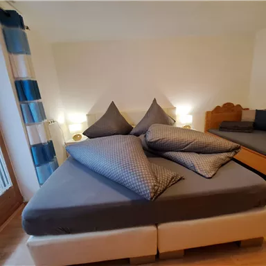 Ein gemütliches Schlafzimmer mit einem großen Bett und zusätzlichen Kissen. Die Wände sind hell und das Zimmer ist freundlich und einladend.