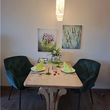 Ein eleganter Essbereich mit einem Holztisch und zwei grünen Stühlen. Auf dem Tisch sind dekorierte Teller und Blumen in einer Vase.