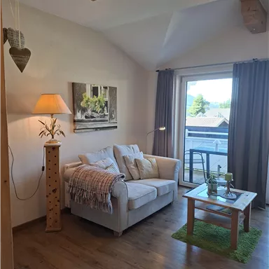 Ein gemütlicher Wohnraum mit einem weißen Sofa und einem kleinen Tisch. Große Fenster lassen viel Licht herein und bieten einen Blick nach draußen.