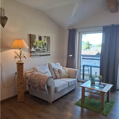 Ein gemütliches Wohnzimmer mit einem weißen Sofa und einer Stehlampe. Große Fenster lassen viel natürliches Licht hereinzufließen.