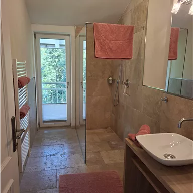 Ein modernes Badezimmer mit einer Dusche und einem Waschtisch. Die Wände sind in neutralen Farbtönen gehalten, und es gibt orangefarbene Handtücher.