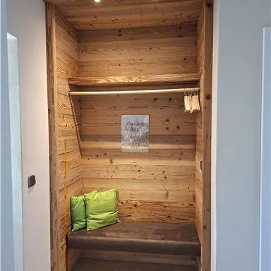 Ein gemütlicher Eingangsbereich mit Holzregalen und einer Bank. Zwei grüne Kissen sorgen für zusätzlichen Komfort.