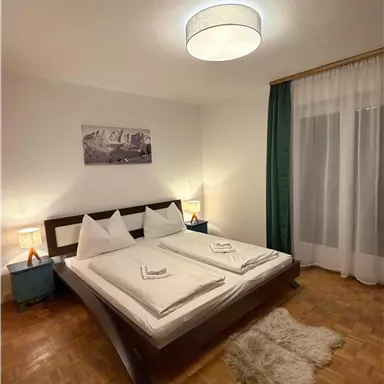 A cozy bedroom with a double bed and two nightstands. Soft lighting and a large window create an inviting atmosphere.