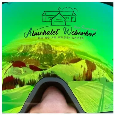 Eine Skibrille mit einer grünen Linse spiegelt die schneebedeckte Berglandschaft wider. Im Hintergrund ist der Wilde Kaiser zu sehen.
