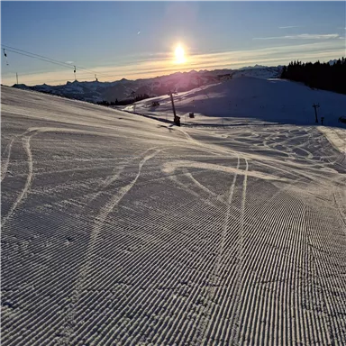 A snowy slope at sunrise. The sky is clear and the tracks in the snow are visible.