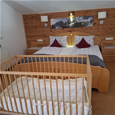 A cozy bedroom with a double bed and a baby crib. The walls are made of wood, and there are decorative elements.