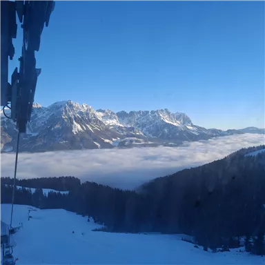 An impressive mountain landscape with snow-capped peaks and a cloud cover in the valley. The sky is clear and brightly blue.