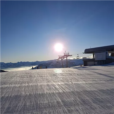 A sunny day on a sparkling slope. In the background, ski lifts and a clear mountain landscape can be seen.