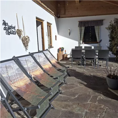 A cozy terrace with lounge chairs and a dining table. In the background, windows and a decorative wall design can be seen.