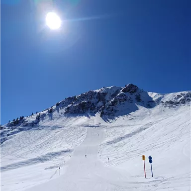 A snow-covered slope under a clear blue sky. In the distance, an impressive mountain can be seen.