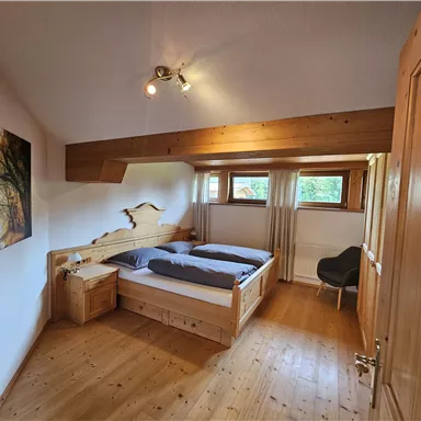 A cozy bedroom with a double bed and wooden floor. There is a window with a view outside and a picture on the wall.