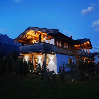 A beautiful house in the evening light, surrounded by greenery. The sky has a gentle twilight with some clouds.