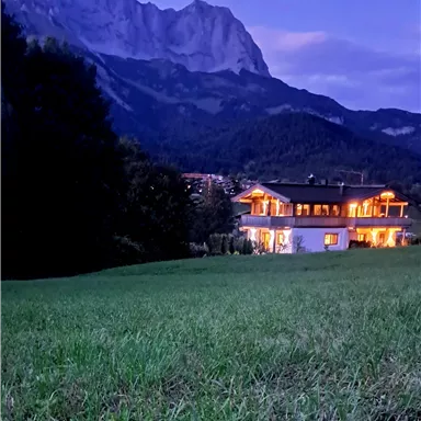 A stylish house in the mountains at twilight, surrounded by meadows. The warm lights of the house shine into the peaceful landscape.