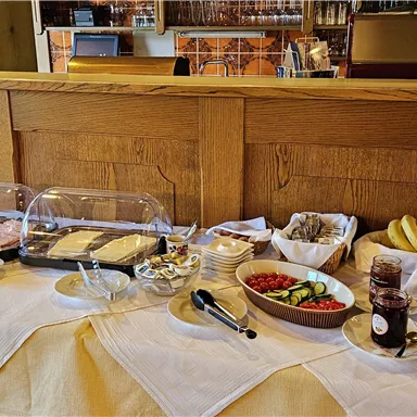 A rich breakfast buffet with fresh bread, cold cuts, fruit, and jam. The table is neatly set and inviting.