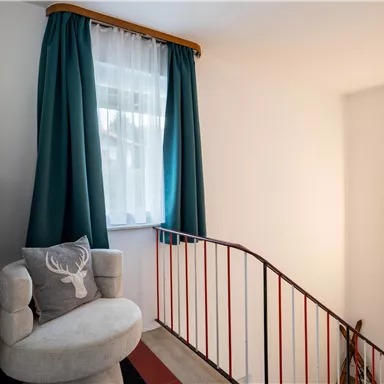 An inviting hallway with a cozy seating area and a window. The walls are light, and the space is accented by a modern lamp and beautiful curtains.