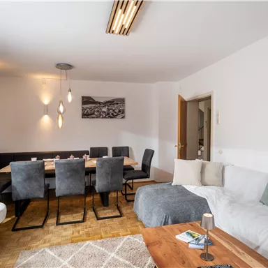 A modern living room with a cozy couch and a dining table for twelve people. The walls are painted light and a large window ensures plenty of light.