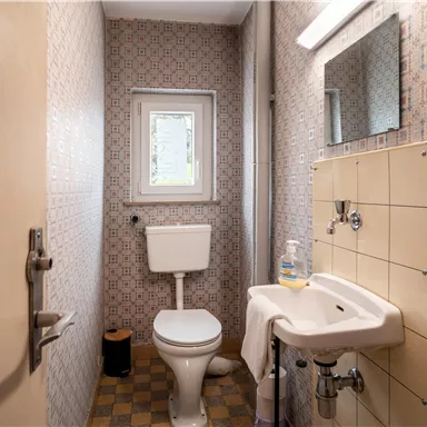 A small bathroom with a toilet and a sink. The walls are decorated with patterned wallpaper.