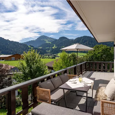A beautiful terrace with comfortable furniture and a magnificent view of green mountains. The sky is clear and the landscape is idyllic.