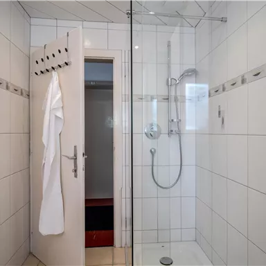 A modern bathroom with a glass shower. White tiles and a towel rack complete the furnishings.