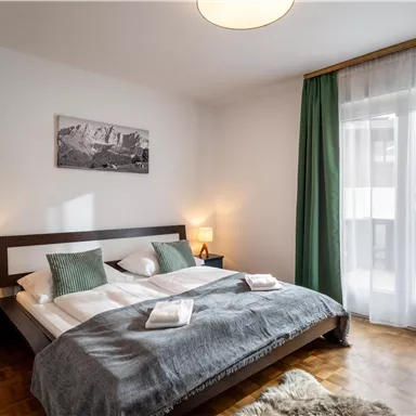 A modern bedroom with a large bed and soft colors. Windows with curtains let in plenty of light and create an inviting atmosphere.