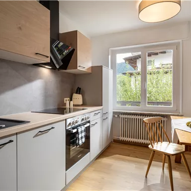 Modern kitchen with wooden and white elements. A table with fruit and large windows creates a bright, welcoming atmosphere.