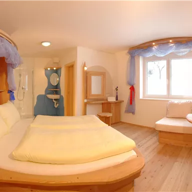 Ein gemütliches Zimmer mit einem runden Bett und Holzverkleidung. Das Licht ist freundlich, und es gibt eine Sitzecke mit einem kleinen Tisch.